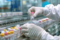 Healthcare Lab Worker Wearing Protective PPE Gloves Examining Medical Vials on Mass Production Conveyor Belt in Pharmaceutical Drug Factory Producing Prescription Medication and Hospital Medicine