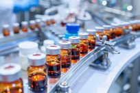 Healthcare production facility with medical vials traveling along the conveyor belt of the pharmaceutical assembly line.